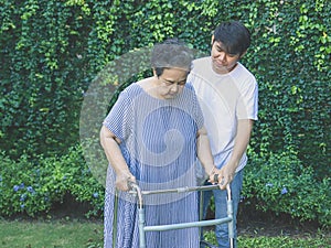 Asian elderly woman walking in the park with orthopedic walker ,helping of her son. Physical activity of old age concept