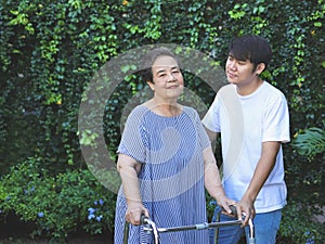 Asian elderly woman walking in the park with orthopedic walker ,helping of her son. Physical activity of old age concept