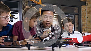 Asian electronic engineer with caucasian schoolchildren working in modern school lab and testing model electric car