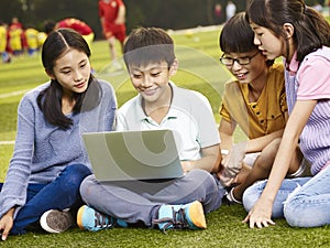 Asian elementary school children using laptop outdoors