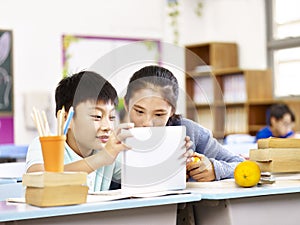 Asian elementary school girl and schoolboy using tablet together