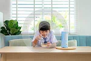 Asian elementary school student girl in uniform eating breakfast cereals with milk in morning school routine for day in life