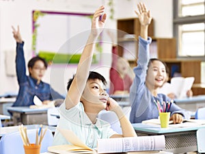 Asian elementary school students raising hands in class