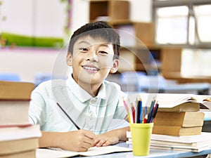 Asian elementary schoolboy doing homework in classroom