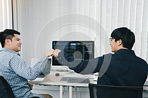 Asian employee software developers celebrate success project by fist bump in office room