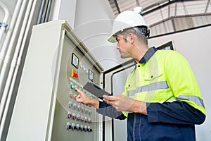 Asian engineer or electrician working on electrical check of water supply system control cabinet with tablet at factory