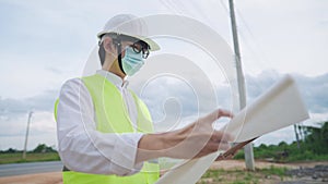 Asian engineer employee wear safety vest helmet looking at construction planner on wireles tablet on outdoor site, civil Engineer