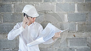 Asian engineer man using phone while reading blueprints