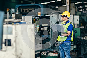 Asian engineer programming the machine in factory with laptop computer to setup program process