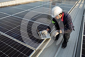 Asian engineer using laptop inspecting solar photovoltaic panels on the roof of an industrial factory. Clean energy concept