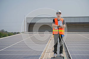 Asian engineer wearing protective vest and white hardhat standing crossed arms on solar panels roof with copy space