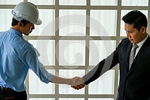 Asian engineer wearing white hard hat with blueprint meeting with business man for project