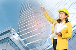 Asian engineer woman with blueprint standing at building background with copy space, engineering construction and architecture