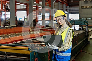 Asian engineer worker inspecting inside the steel manufacturing factory while looking at the laptop for monitoring the improvement