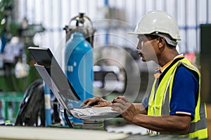 Asian engineer or worker is using a computer to control a steel laser cutting machine in a factory. Real worker