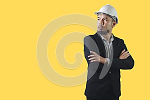 Asian engineering man wears black suit crosse arm white hardhat isolated on yellow background.
