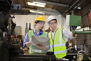 Asian engineering manager and mechanic worker in safety hard hat and reflective cloth using lathe machine in the factory