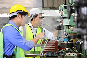 Asian engineering manager and mechanic worker in safety hard hat and reflective cloth using lathe machine in the factory