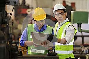 Asian engineering manager and mechanic worker in safety hard hat and reflective cloth using lathe machine in the factory