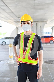 Asian engineering worker wear hard hat and protection vest look around while standing in the parking.
