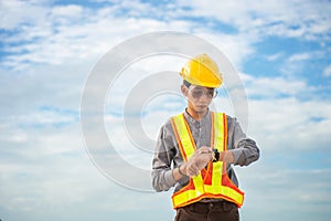 Asian engineering worker wearing hard hat glasses and protection vest looking the watch while standing on the cloud background photo