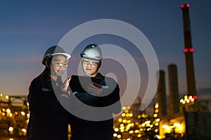 Asian engineers, man and woman are checking the maintenance of the oil refinery factory at night via digital tablets