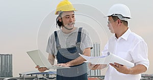 Asian engineers standing on rooftop, young engineer use notebook to discuss about blueprint whit the older.