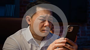 Asian ethnicity 40s man at night evening home office holding mobile phone feel unhappy negative emotions upset by
