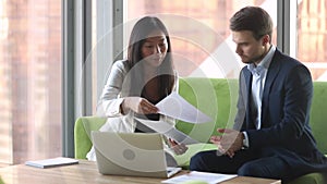 Asian european business partners sitting on couch discussing contract details