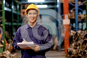 Asian factory man or warehouse worker with smiling hold clipboard and write data of product quality also look to camera in