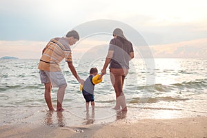 Asian family with 2 years old toddler baby boy child walking barefoot on the beach in water at sunset