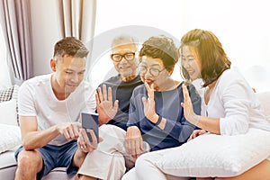 Asian family with adult children and senior parents making a video call and waving at the caller at home. photo