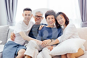 Asian family with adult children and senior parents relaxing on a sofa at home together.