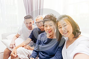 Asian family with adult children and senior parents taking selfie and sitting on a sofa at home. Happy and relaxing family time