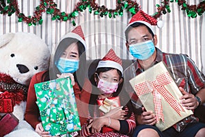 Asian family in Christmas interior.Happy mother father and  daughter wearing face mask and holding a gift box with smile