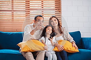 Asian family consisting of happy parents and daughter watching TV or movie together on sofa in living room at home. enjoy relaxing