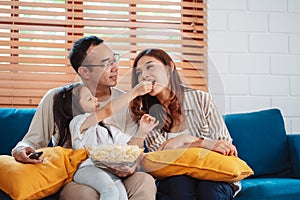 Asian Family consisting of parents, happy daughter watching TV or movie