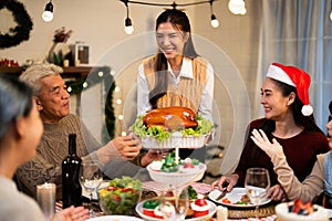 Asian family cousin woman smile while serving roasted turkey meal in white dish on the table with enjoyment for winter festival