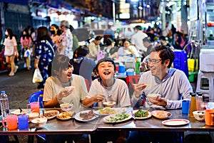 Asian family enjoy eating food on street food restaurant with crowd of people at Yaowarat road, Bangkok