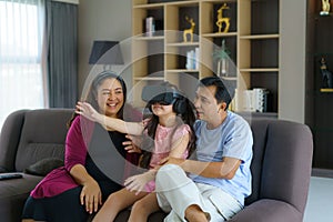 Asian family enjoy technology device hand use vr goggle glasses play fun together on sofa living room at home. Smart technology