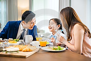 Asian family father, mother with children daughter eating breakfast food on dining table kitchen in mornings