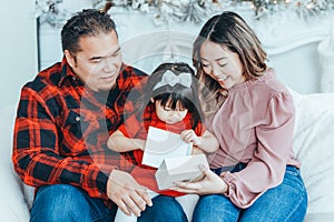 Asian family father, mother giving gift box with present to daughter toddler girl celebrating Christmas or New Year