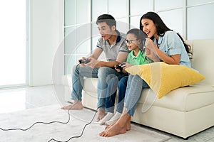 Asian family father and son having fun playing computer console games together in living room at home with handset controllers and