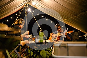 Asian family and friends vacation camp, Dinner and relaxing guitar play under tarp or flysheet, Outdoor camping on the courtyard