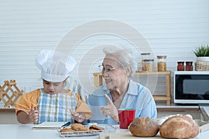 Asian family grandmother and grandchild have fun cooking at home kitchen together, little cute granddaughter with chef hat