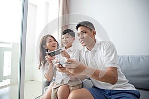 Asian family having fun playing computer console games together, Father and son have the handset controllers and the mother is ch