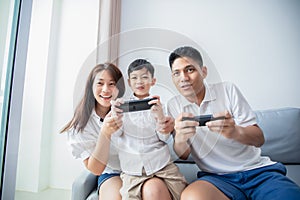 Asian family having fun playing computer console games together, Father and son have the handset controllers and the mother is