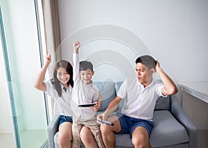 Asian family having fun playing computer console games together, Father and son have the handset controllers and the mother is