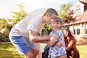 Asian Family Having Fun In Summer Garden At Home With Children Playing Together