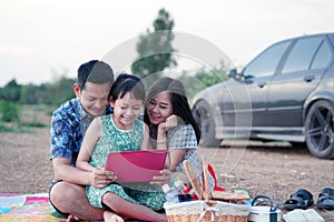 Asian family having a picnic and looking laptop in the park with smile and happy